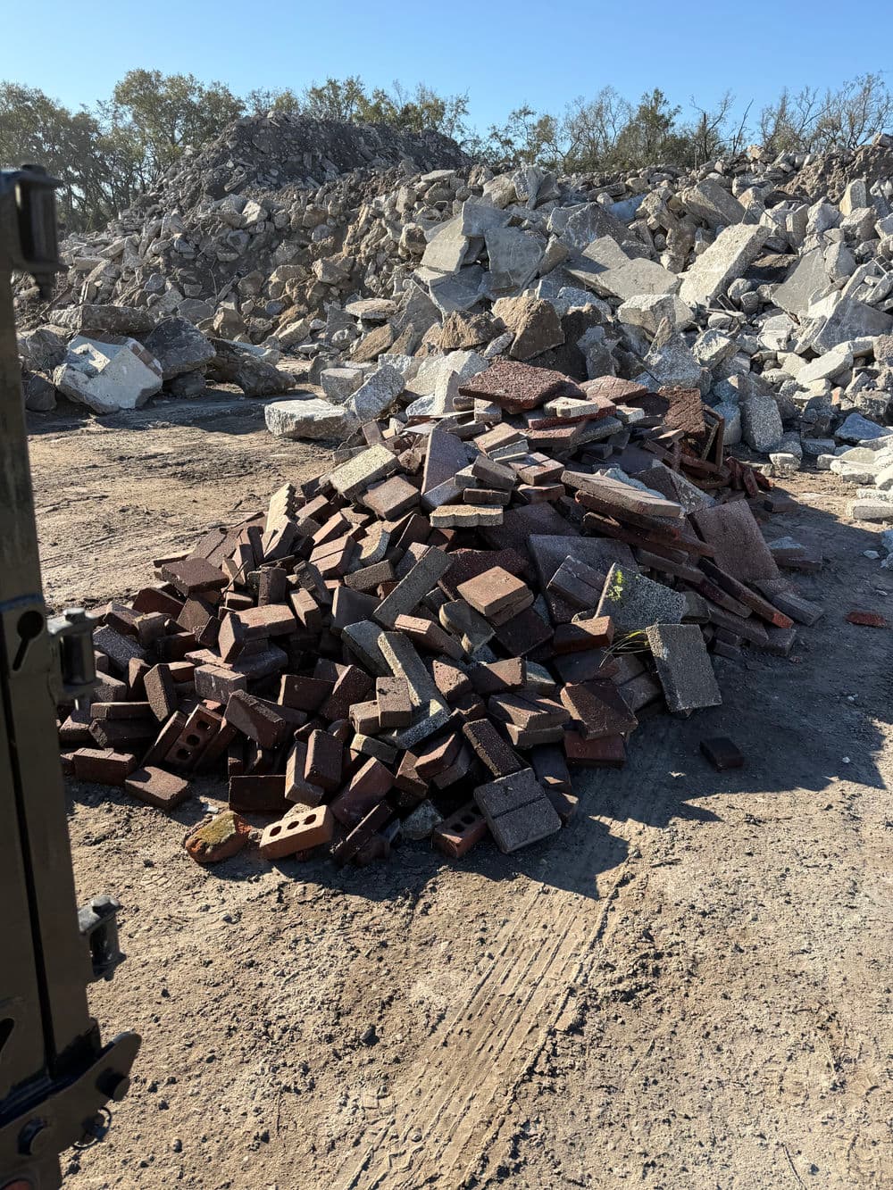 Piles of red bricks and stone debris at a construction site under clear blue skies.