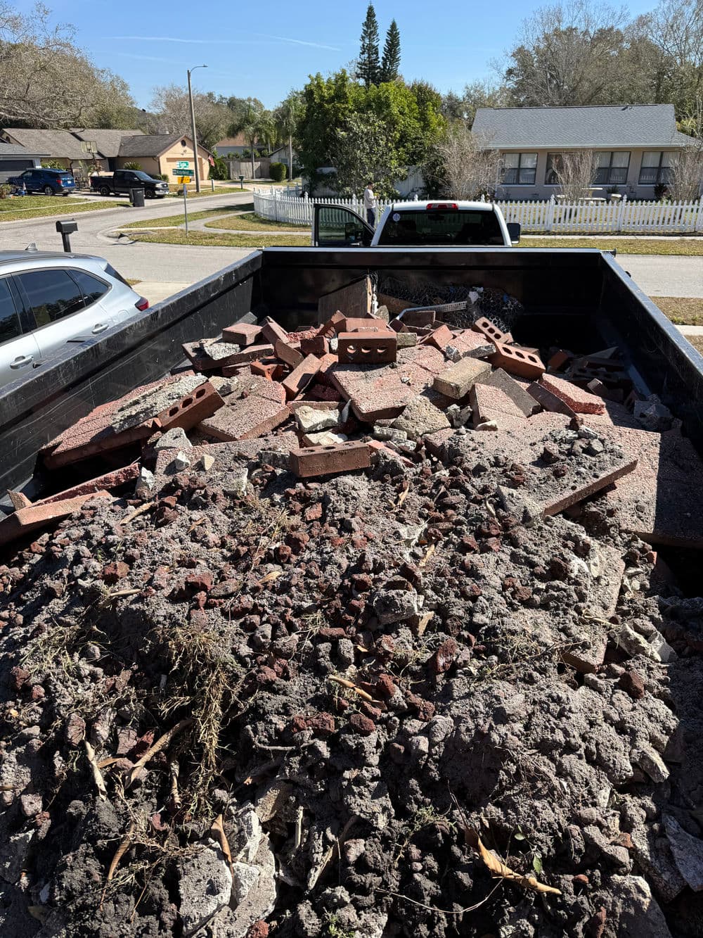 Truck bed filled with construction debris, including bricks and concrete rubble, in residential area.