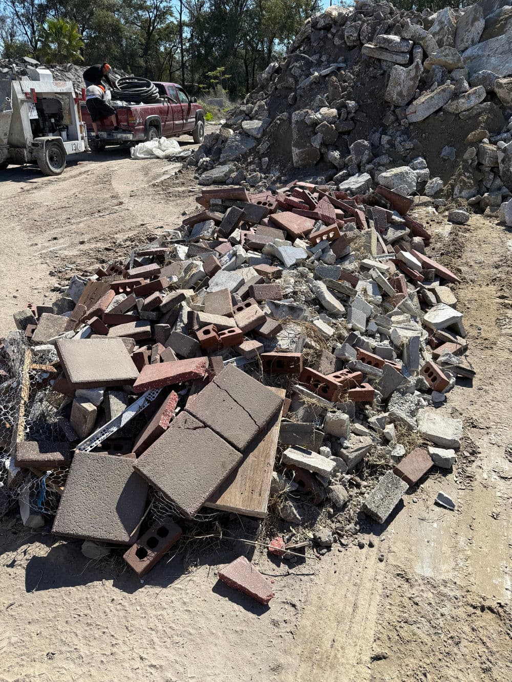 Piles of broken bricks and debris at a construction site, with a truck in the background.
