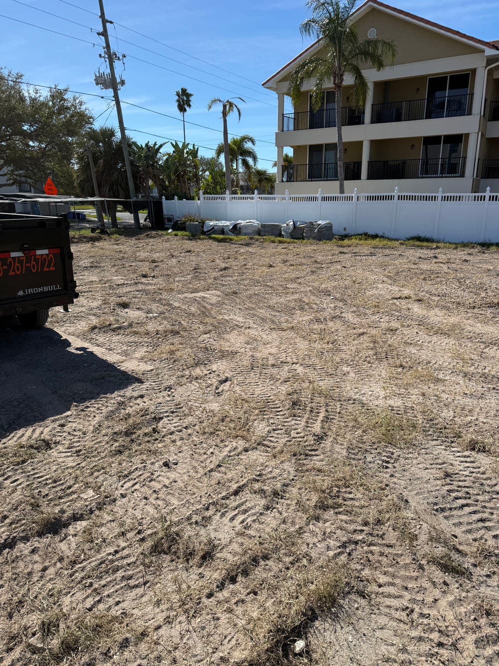Cleared lot for development with construction materials and palm trees in the background.