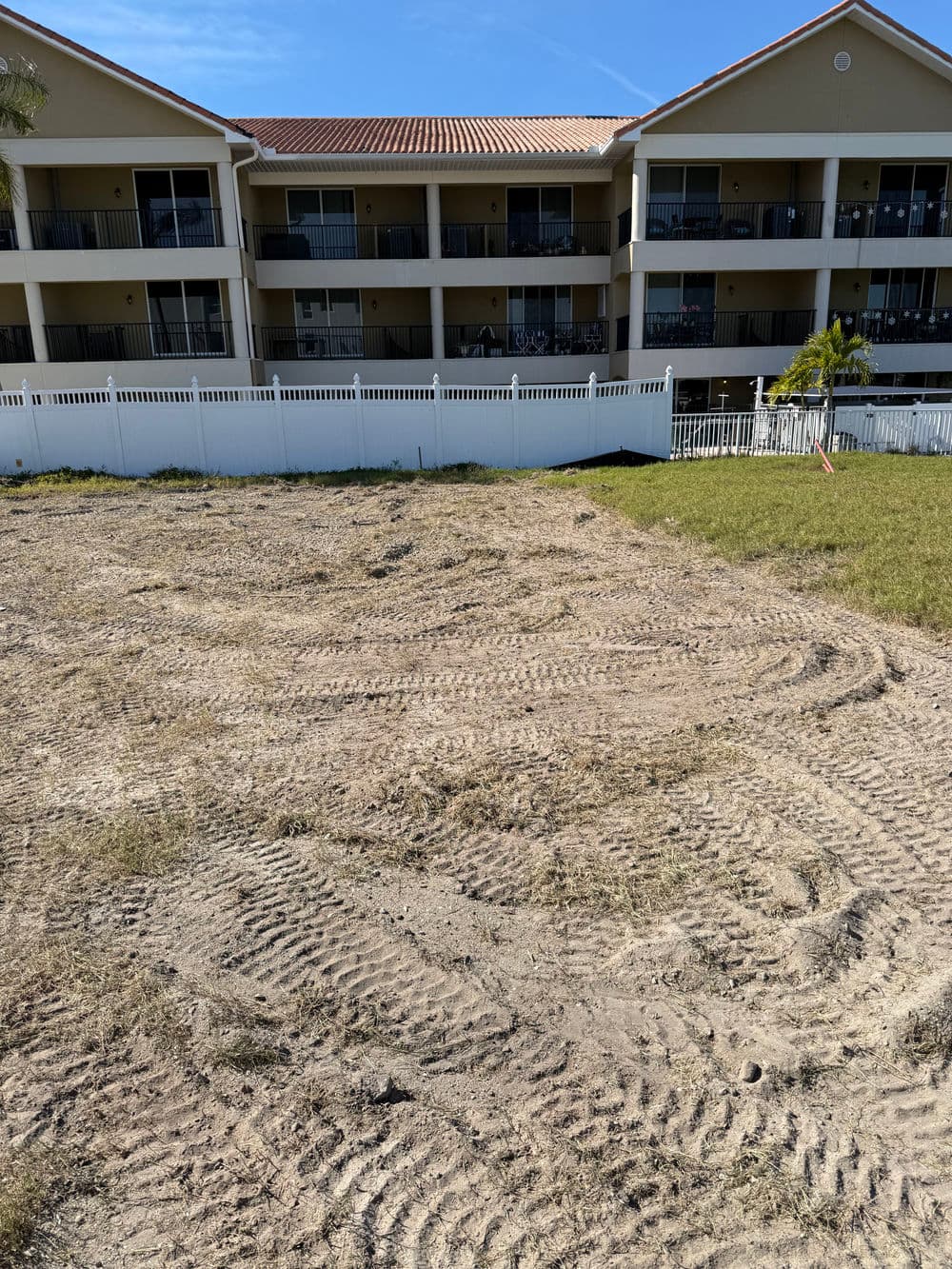 Empty lot with tire tracks, grass patches, and a multi-story apartment building in the background.