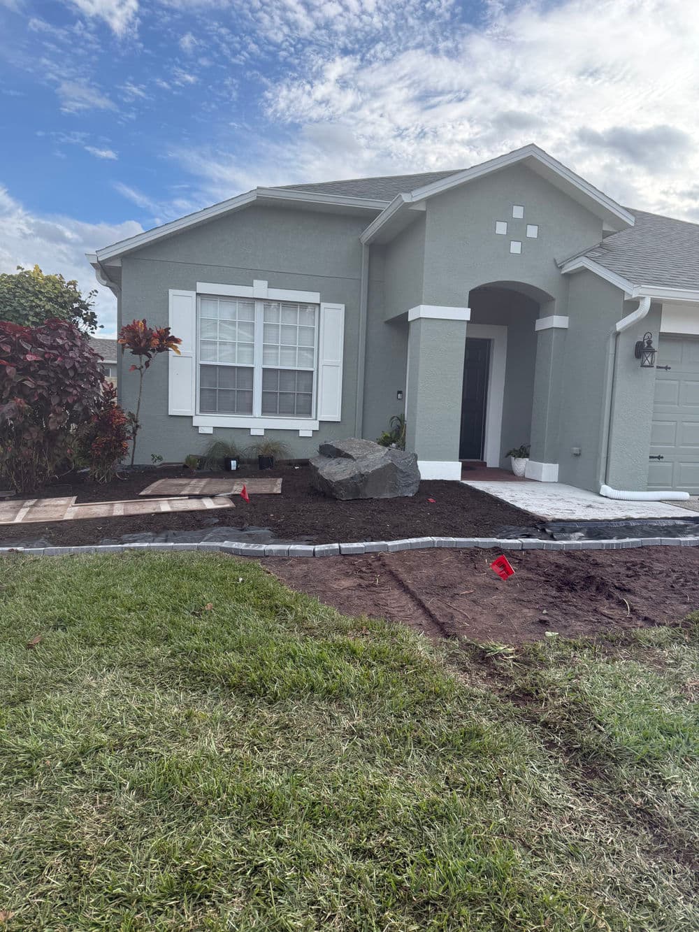 Landscaped front yard of a gray house with new plants, a large rock, and fresh grass.