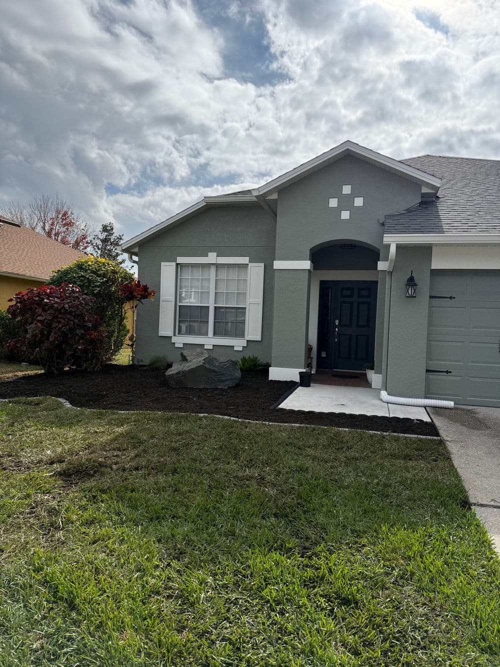 Gray house with decorative stone, green lawn, and cloudy sky. Landscaping in progress.