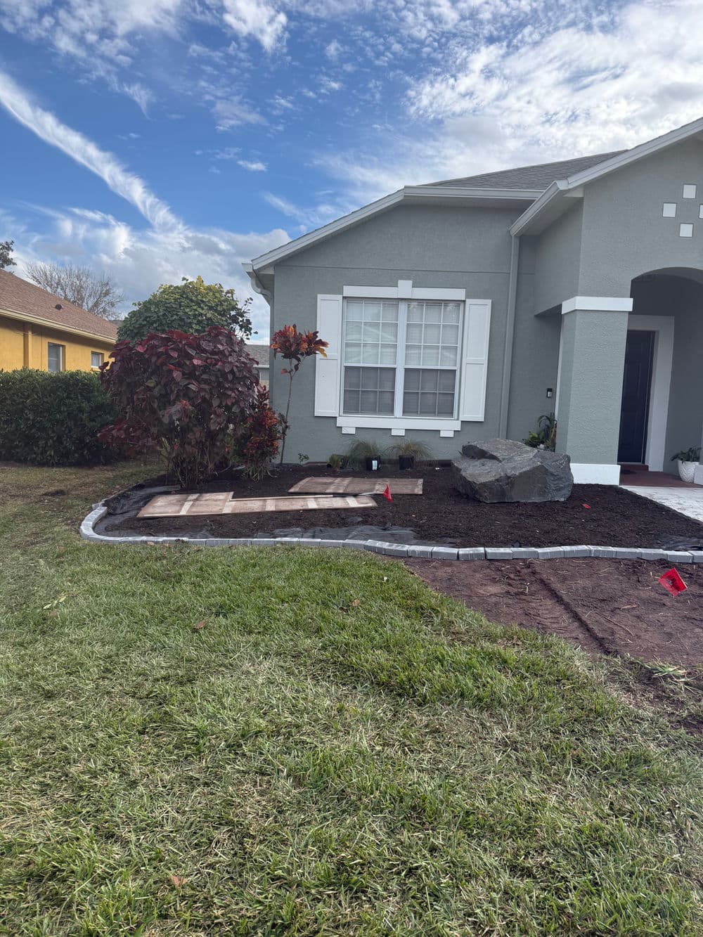 Landscaped front yard featuring new stone pathway and colorful shrubbery under a blue sky.