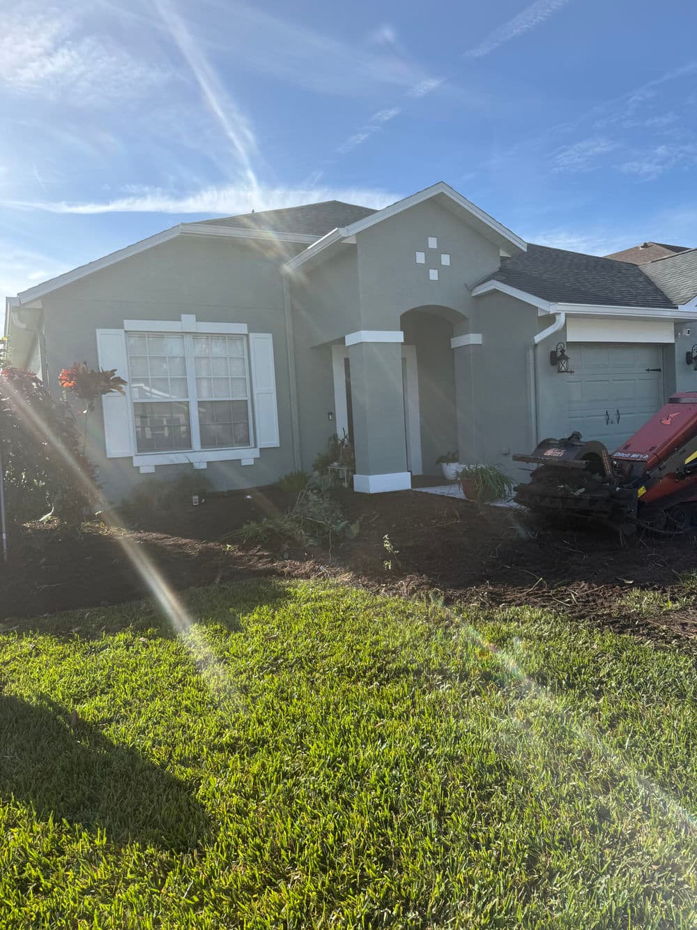 Front view of a modern gray house with a well-maintained lawn and landscaping work in progress.