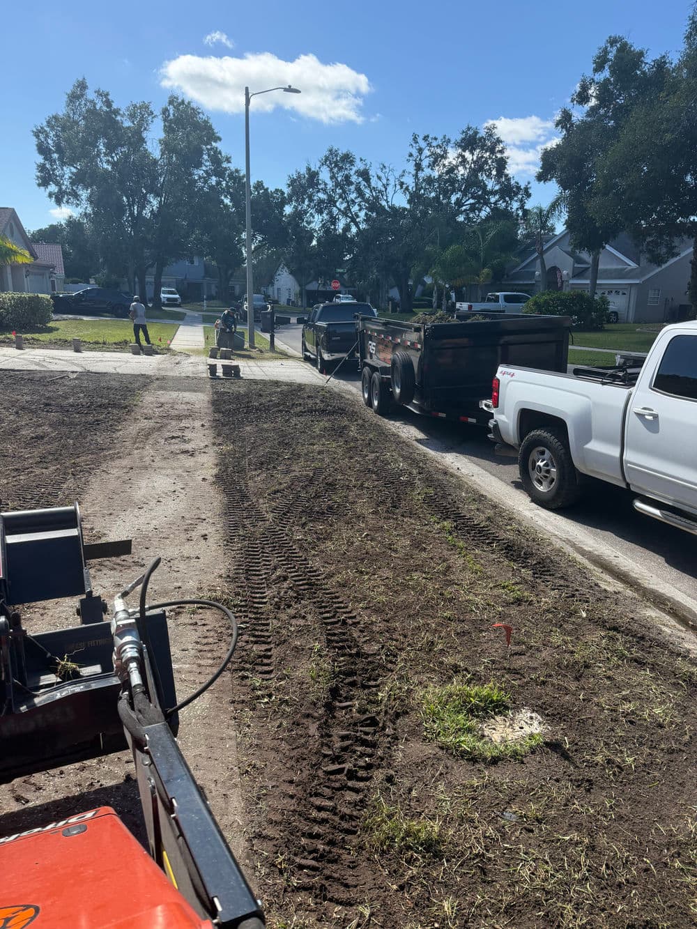 Construction scene showing trucks and machinery on a residential street with freshly dug earth.