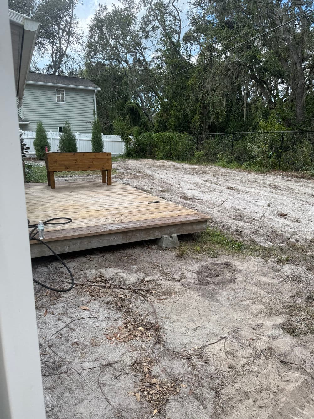 Wooden deck in a landscaped yard with cleared ground and trees in the background.