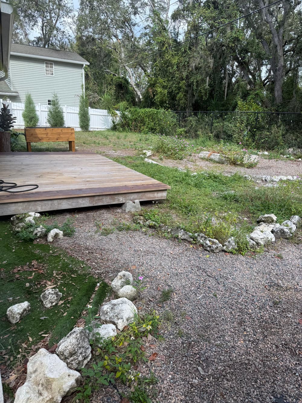 Backyard garden with wooden deck, native plants, and gravel path surrounded by trees.