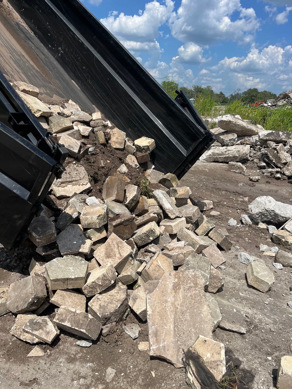 Dump truck unloading large rocks and gravel at a construction site under a blue sky.