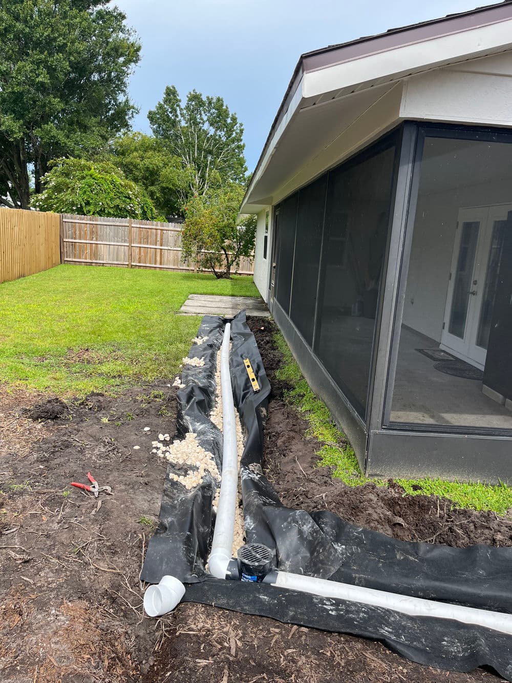 Drainage system installation in backyard with landscaping fabric next to a house.