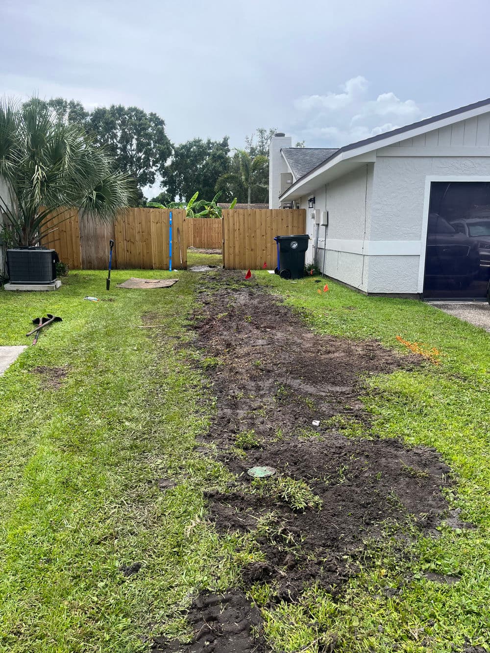 Cleared dirt area in yard for landscaping, with tools and fence in background.