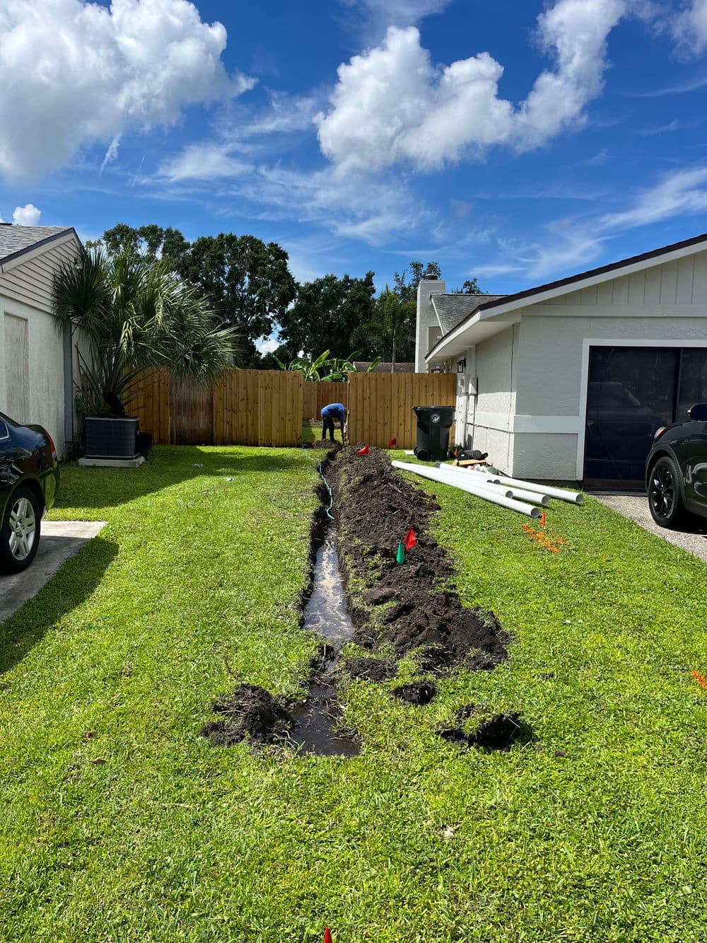 Man digging a trench in a residential yard for landscaping or drainage installation.