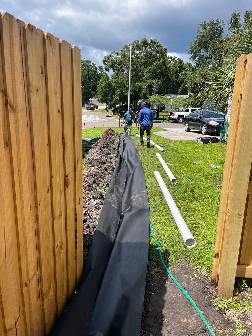 Workers laying landscaping fabric along a garden bed beside a wooden fence.