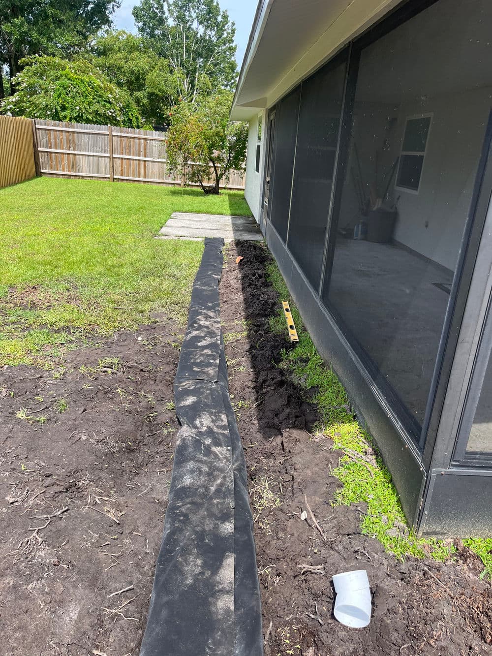Backyard landscape with black landscaping fabric laid out next to a house and a green lawn.