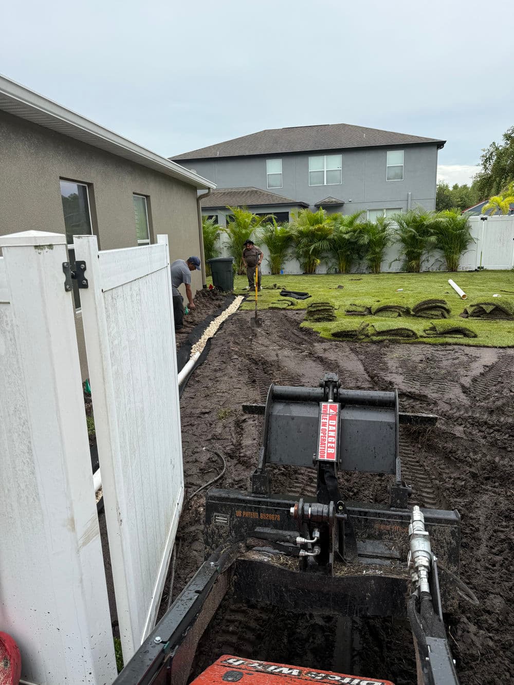 Landscaping project in progress, featuring a machinery and workers laying sod in a muddy yard.