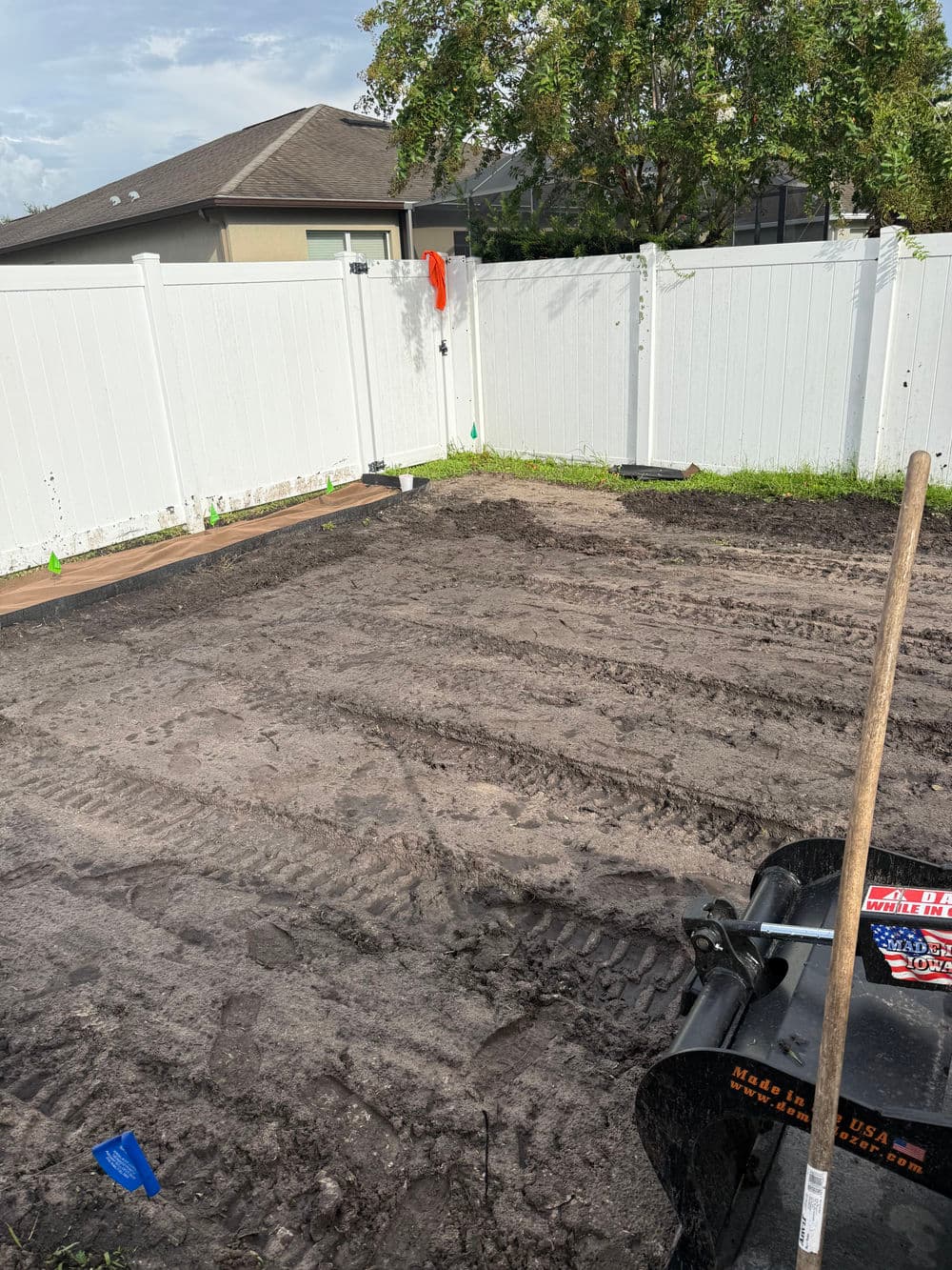 Excavated garden plot ready for planting, with garden tools and a fenced backyard.