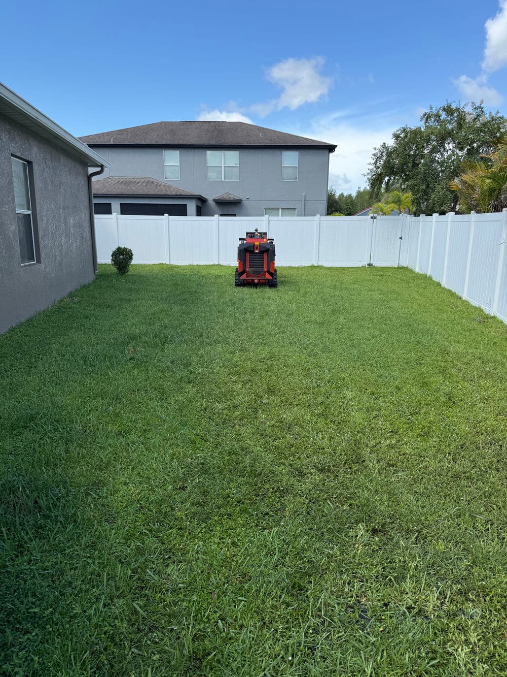 Lawn mower on freshly mowed green grass in a residential backyard with white fence.