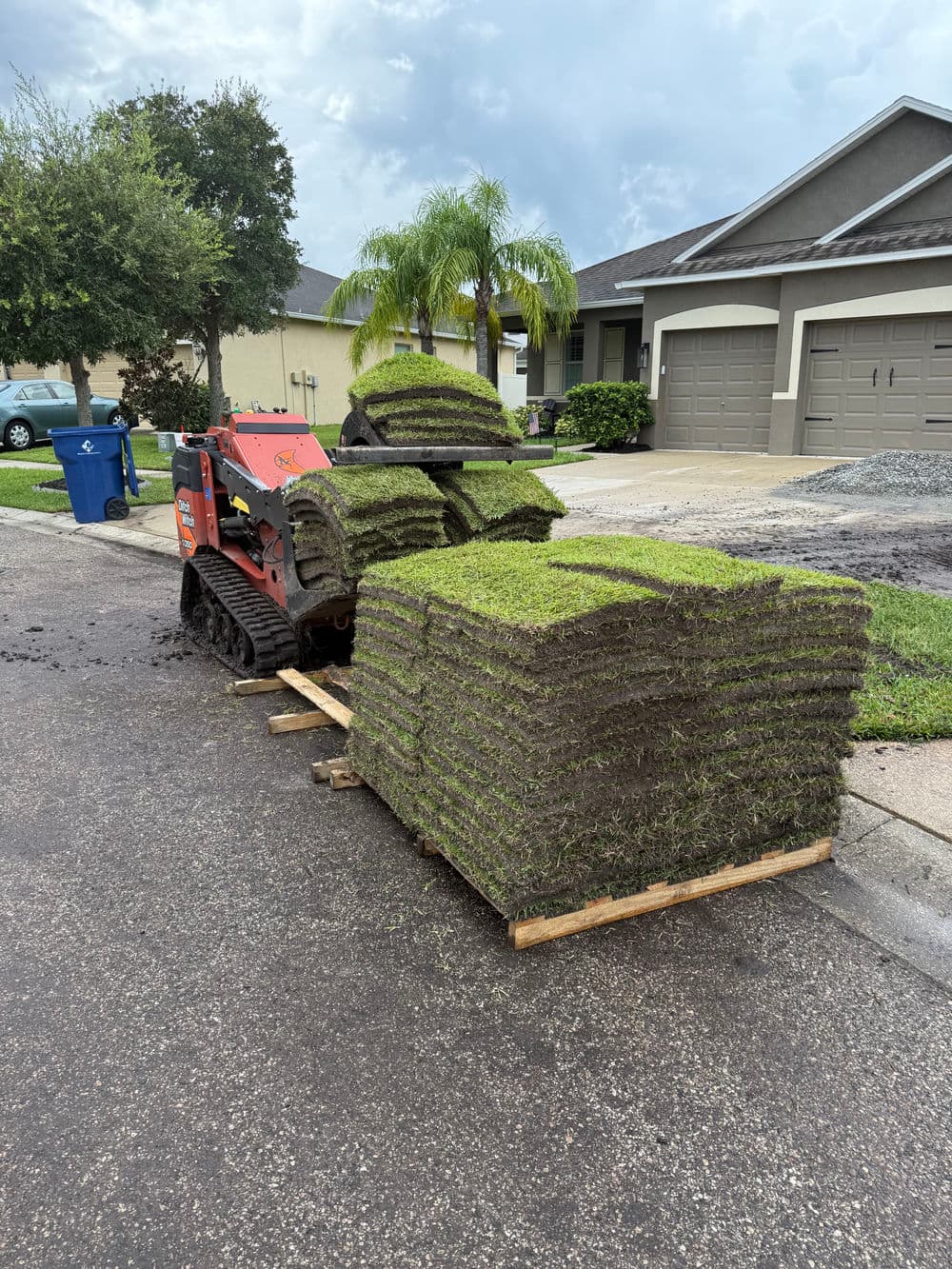 Lawn installation project with sod being transported on a pallet by a small tractor.