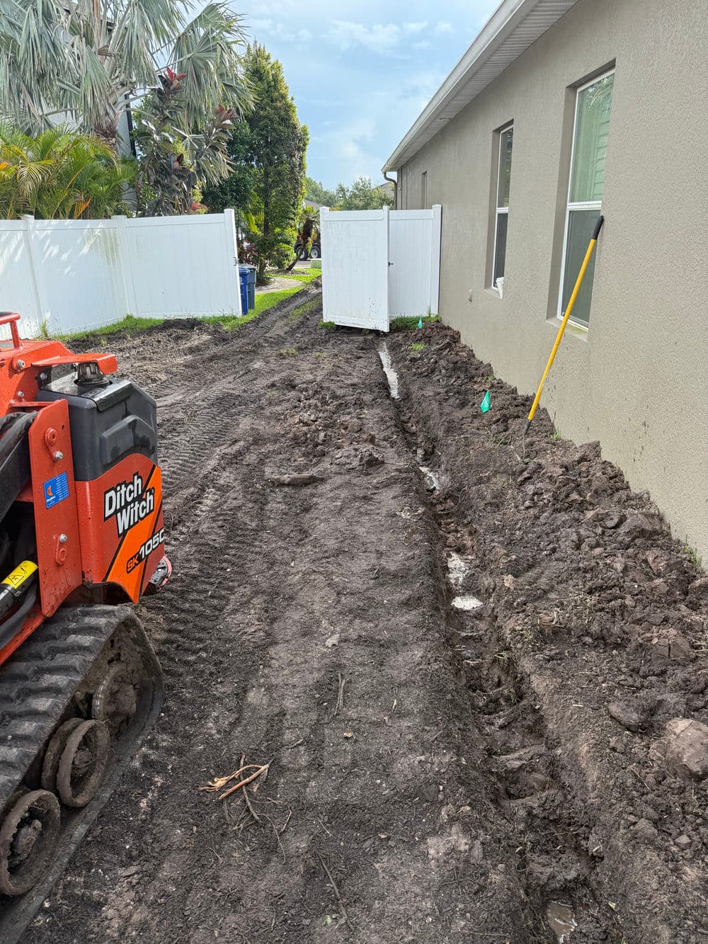 Excavation project with Ditch Witch, showing trench alongside house for drainage systems.