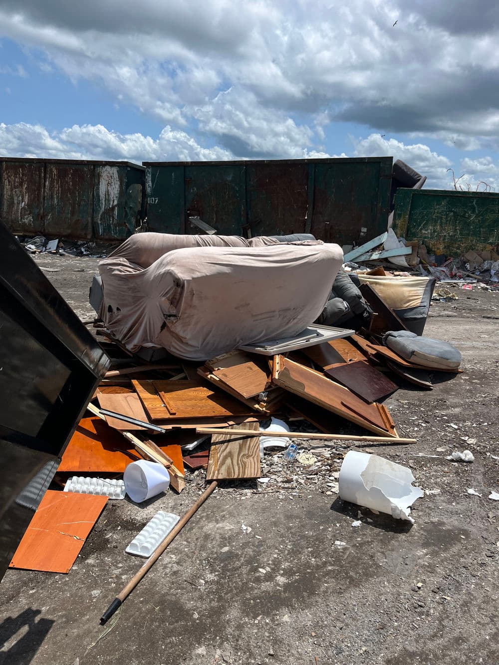 Debris and furniture piled in a landfill under a cloudy sky.