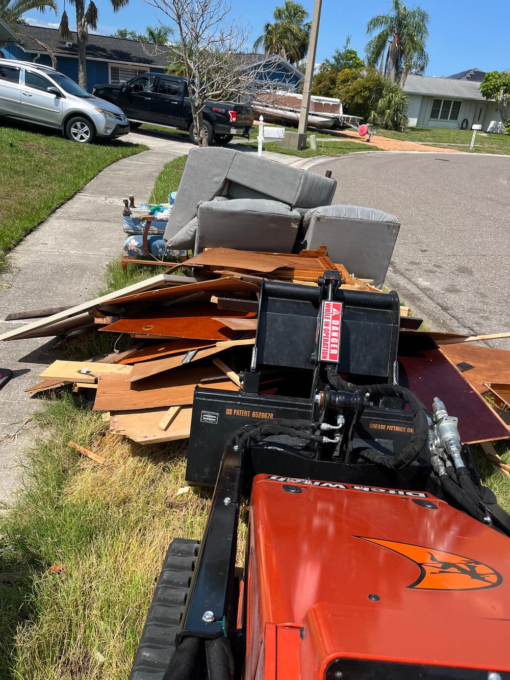 Waste disposal pile with furniture, wood debris, and a small tractor on residential street.