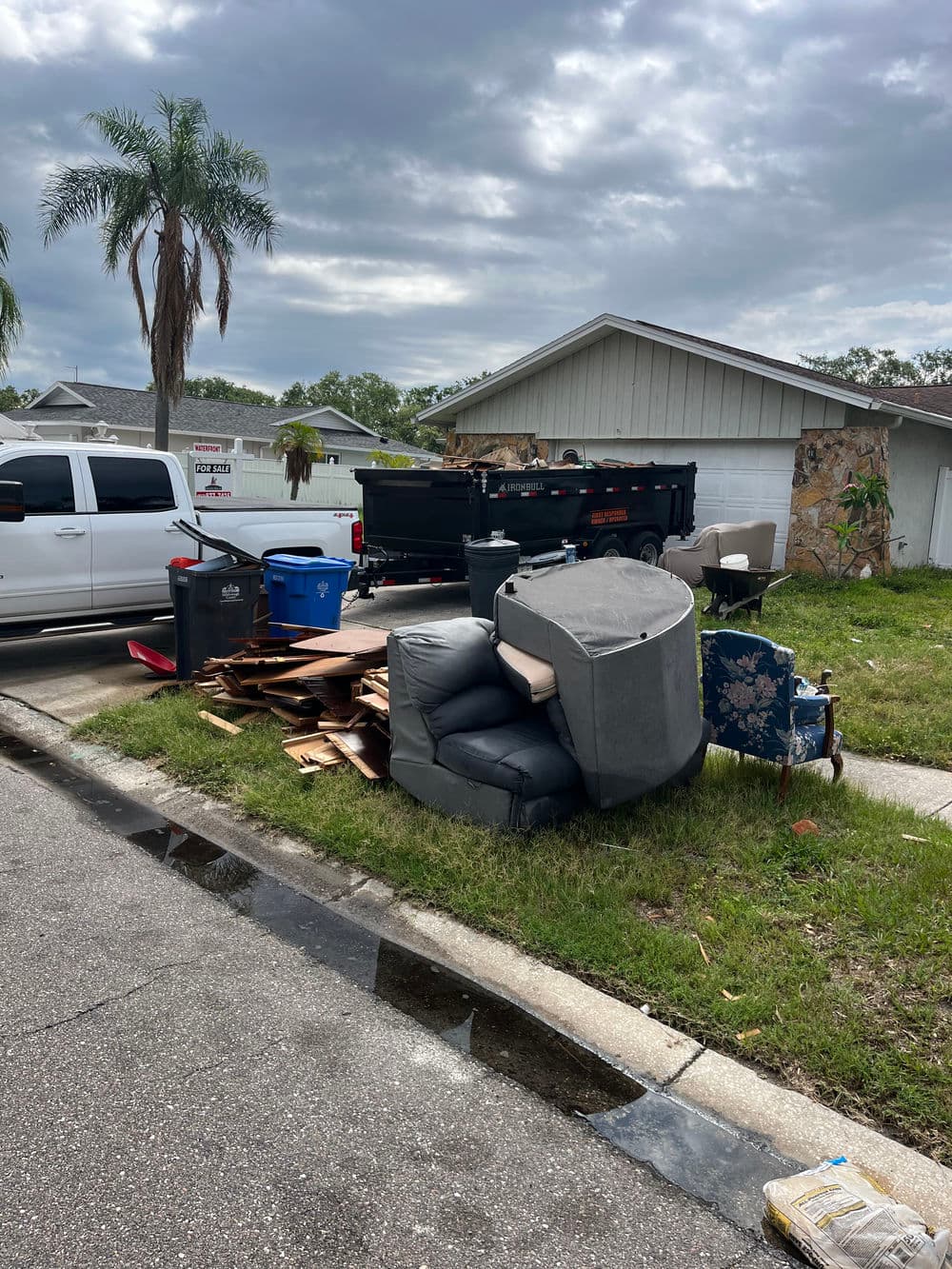Debris and furniture piled on curbside in residential area, with vehicles nearby.