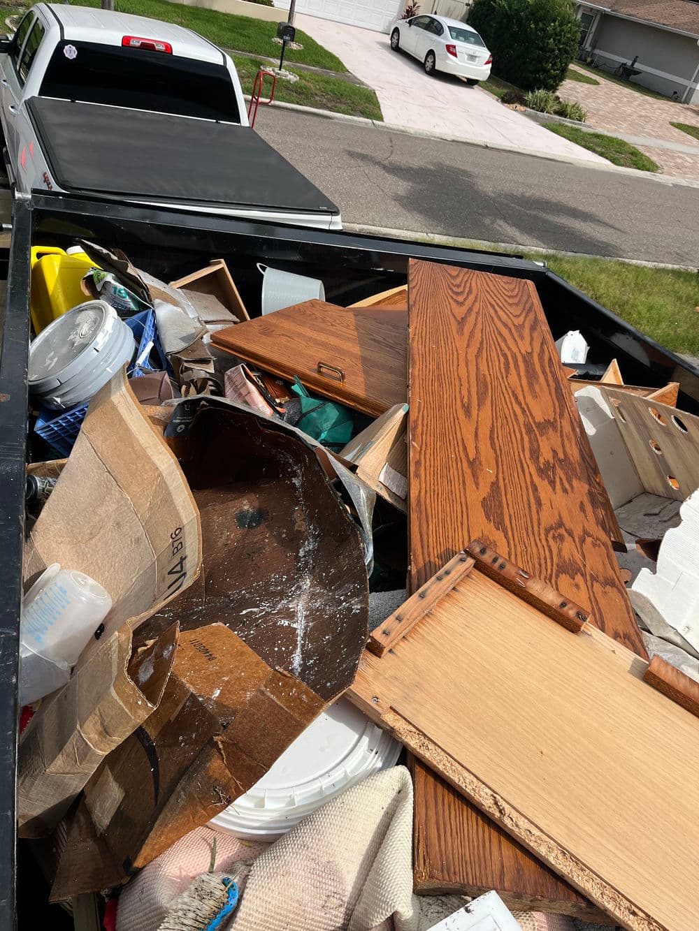 Pickup truck bed filled with discarded furniture, wood pieces, and various household items.