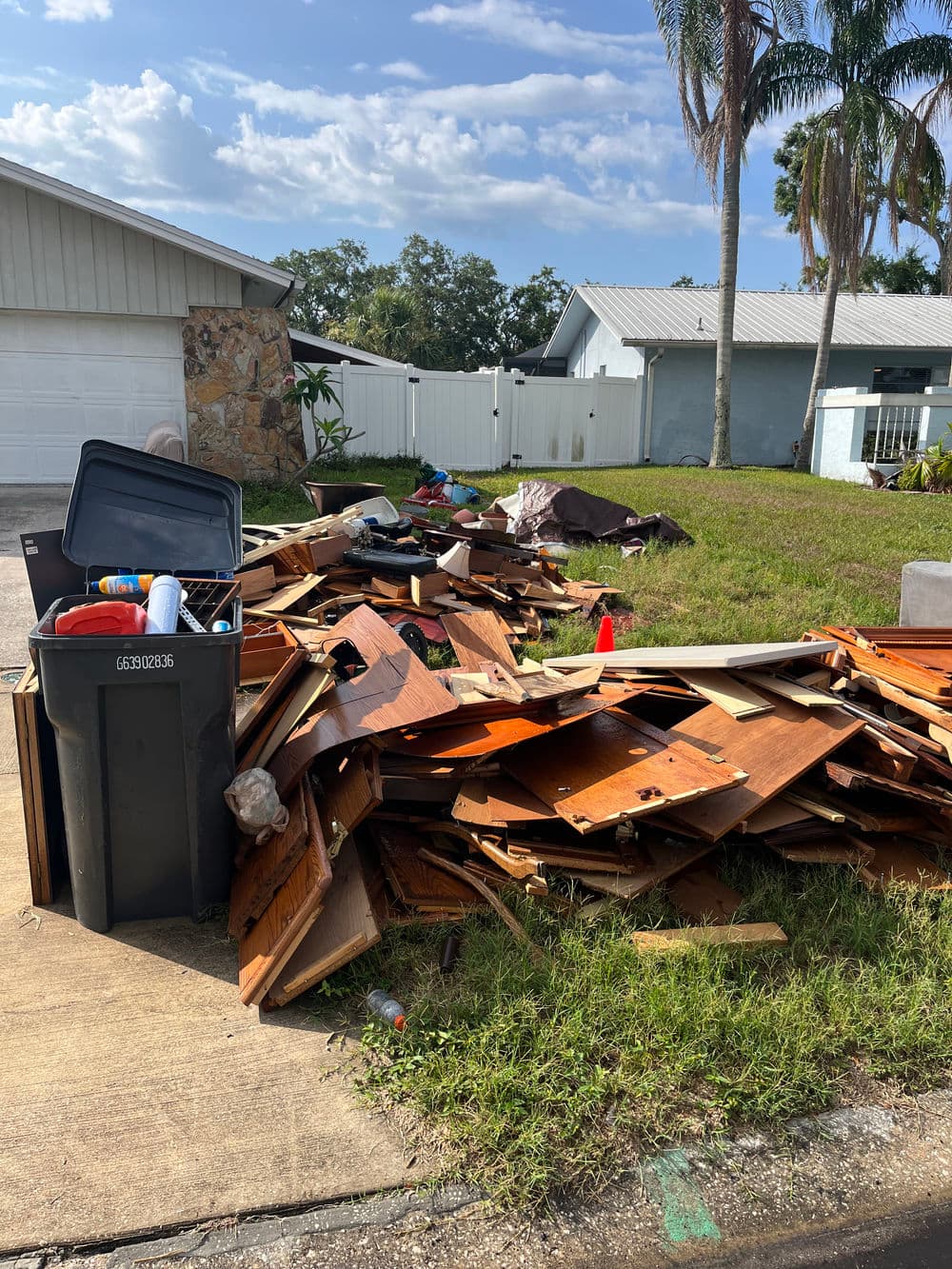 Pile of debris and wooden planks with trash bins on a residential street.