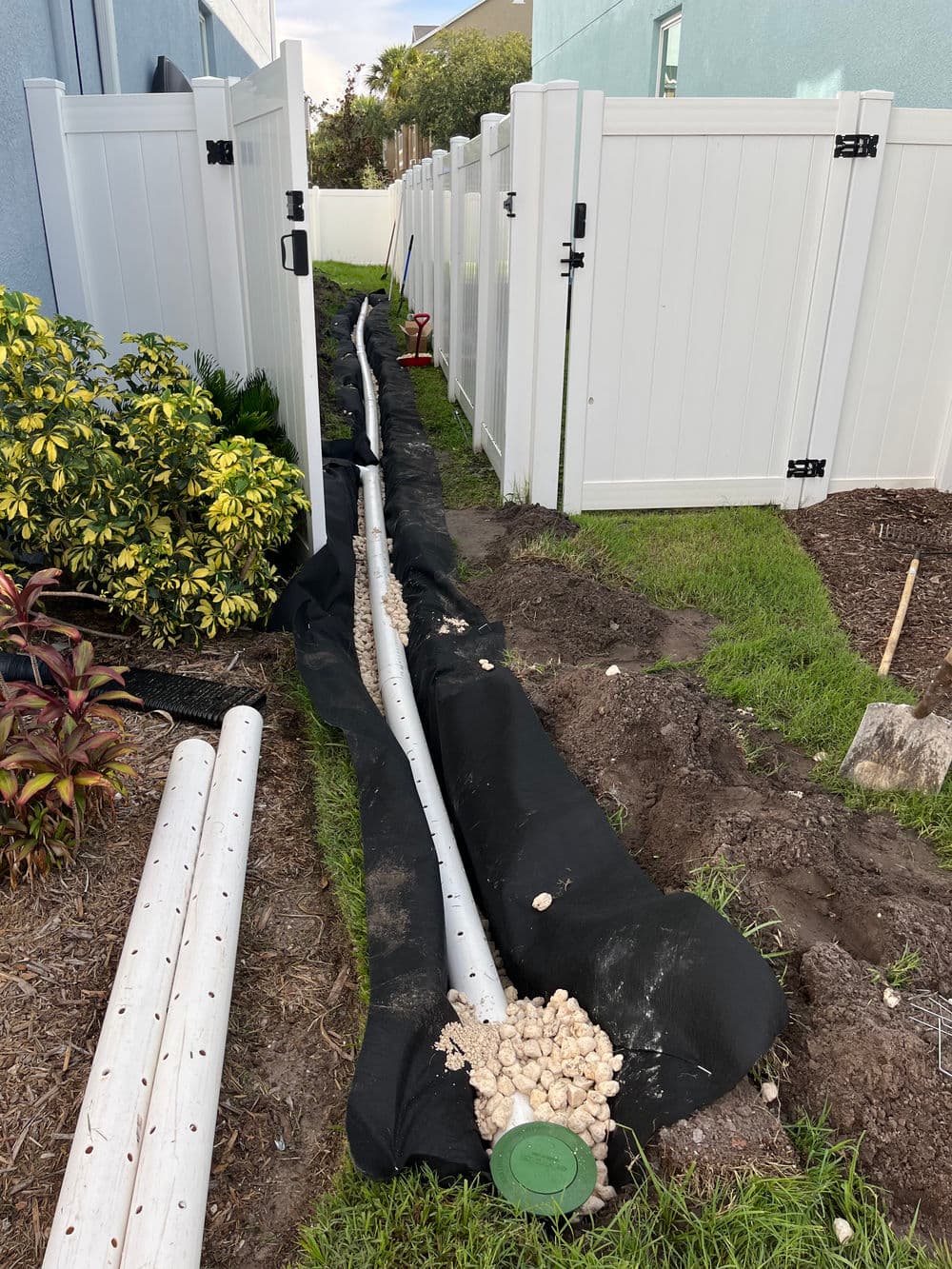 Drainage system installation in a backyard with pipes, gravel, and landscaping.